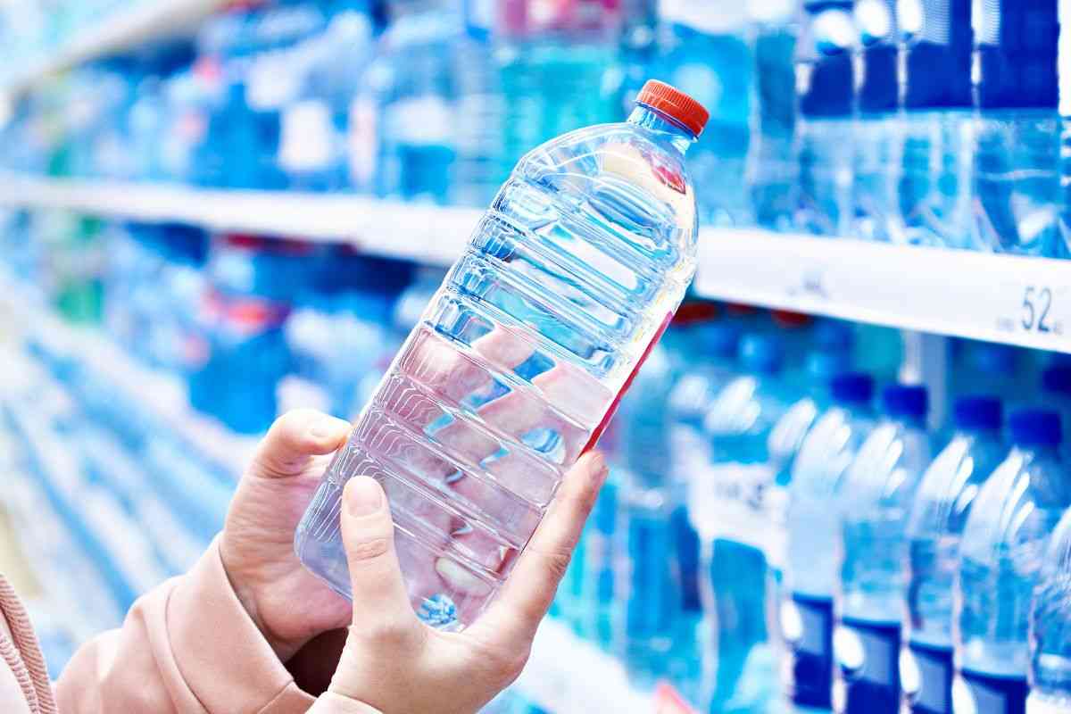 persona che prende una bottiglia di acqua al supermercato